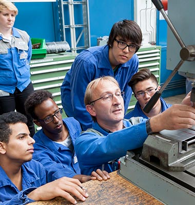 Instructor Alfons Kimberger shows a group of young refugees how to operate a drill (photo)