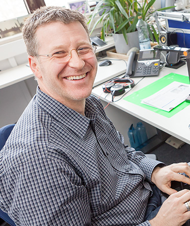 Stefan Kaiser at his desk.He is using various technical aids. (photo)