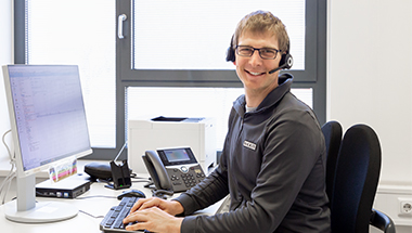 Ein Mitarbeiter am Bereitschaftstelefon sitzt mit Headset an einem Schreibtisch. (Foto)